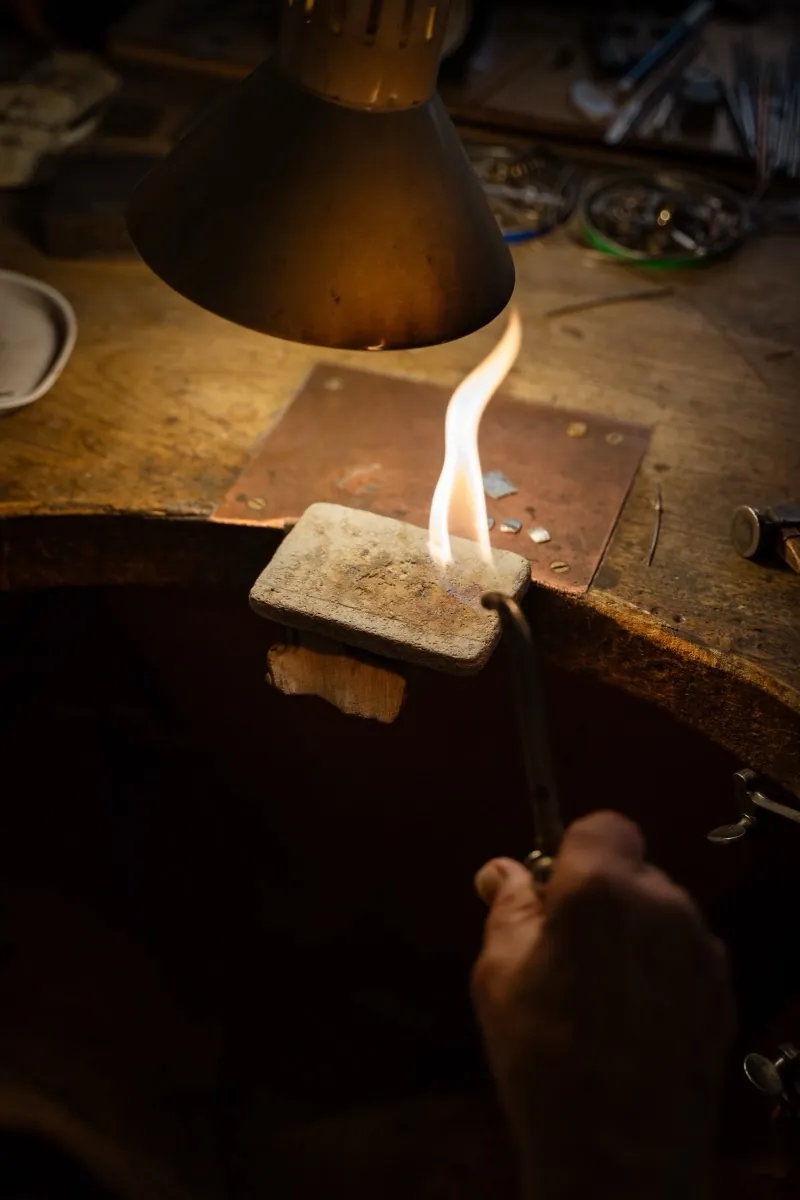 Goldschmied lötet mit offener Flamme an der Werkbank